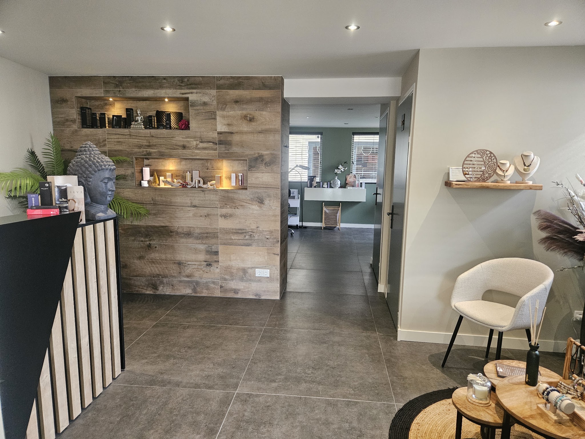 De ontvangstruimte: houten wand met verlichte productplanken, een crèmekleurige stoel en ronde bijzettafels